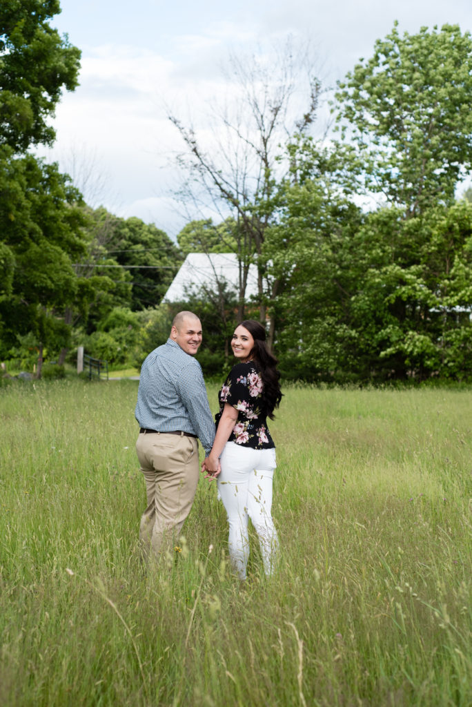 couple walking in a field holding hands looking at photographer