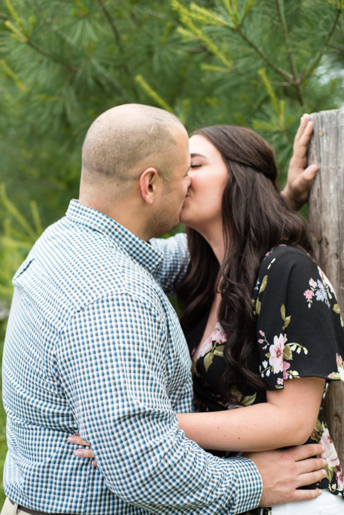 couple kissing leaning against a fence post