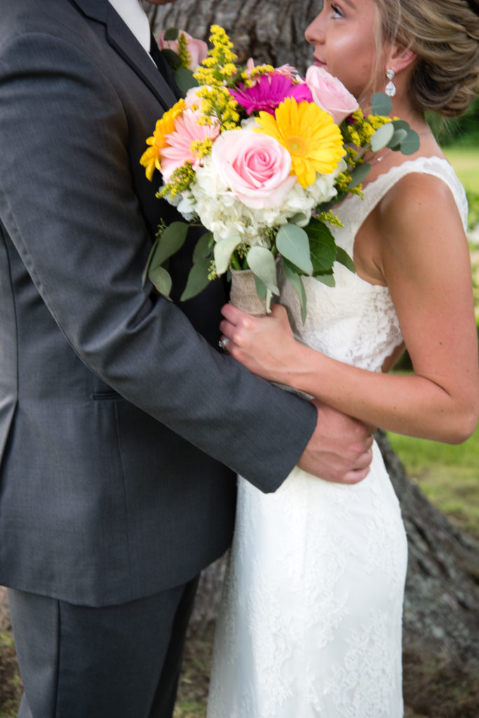 Bride and groom snuggled in close with focus on bouquet and rings