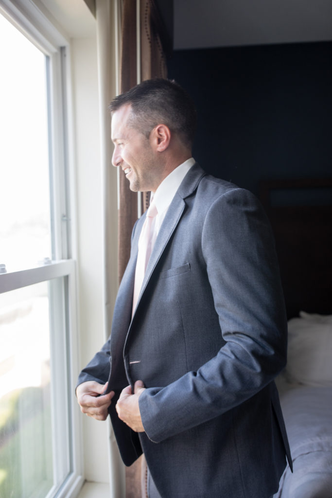 groom looking out the window while buttoning jacket