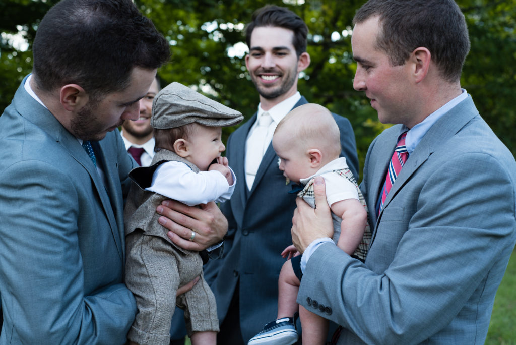 bride's brothers holding the babies facing each other, groom smiling in the background