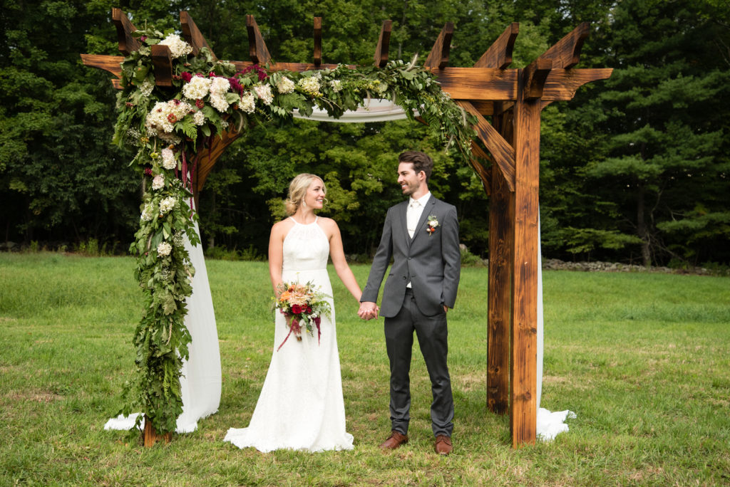 bride and groom standing under ceremony arbor holding hands