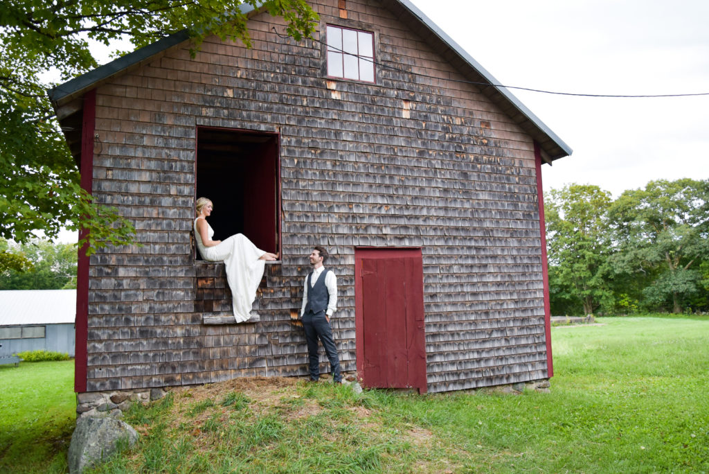 bride sitting in upper barn door looking down at groom 