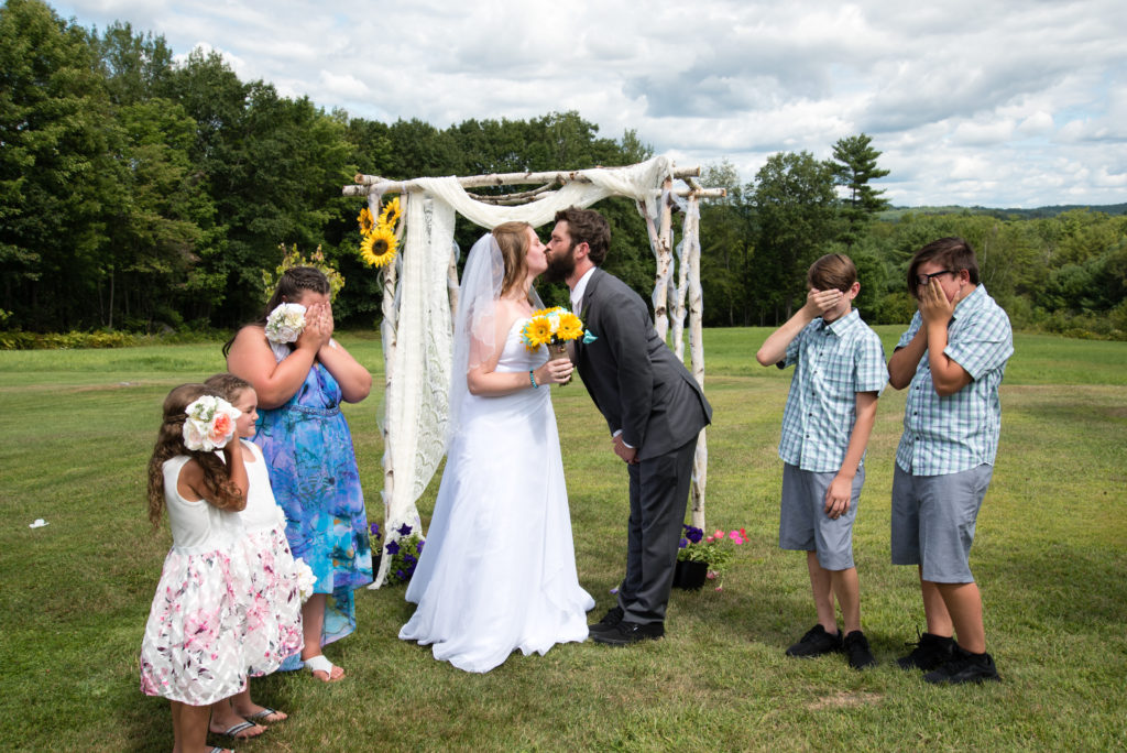 bride and groom kissing while kids cover their eyes