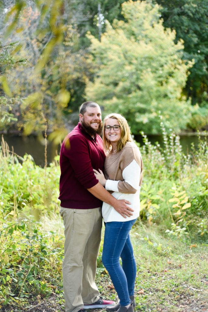 man and woman hugging looking at the camera in front of a pond