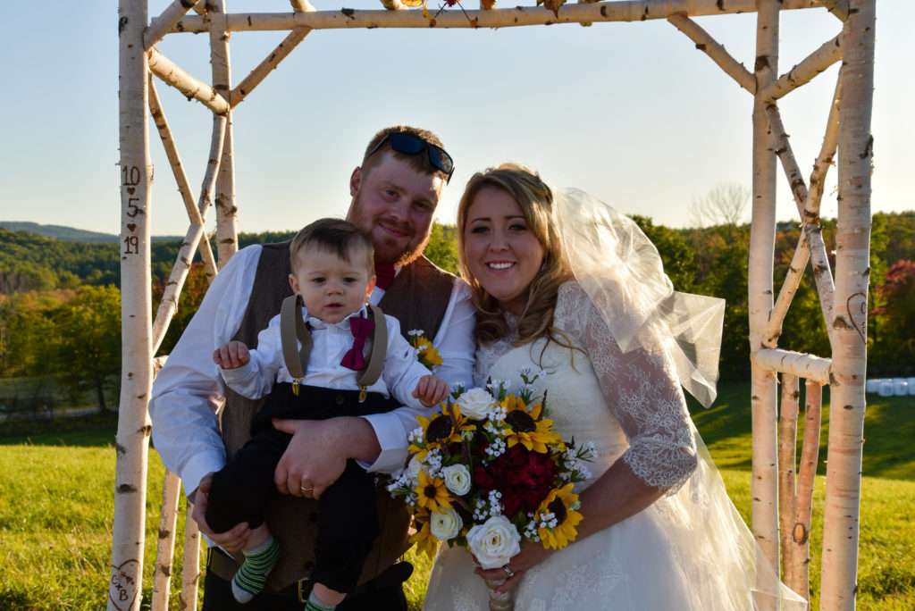 Bride and groom in front of arbor with son