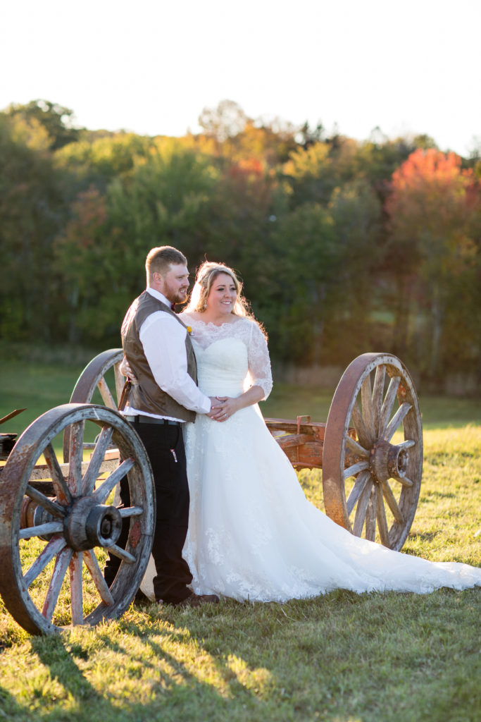 bride and groom posing with wagon in hay field side angle
