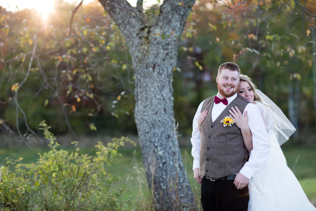 bride and groom posing in field near a tree 