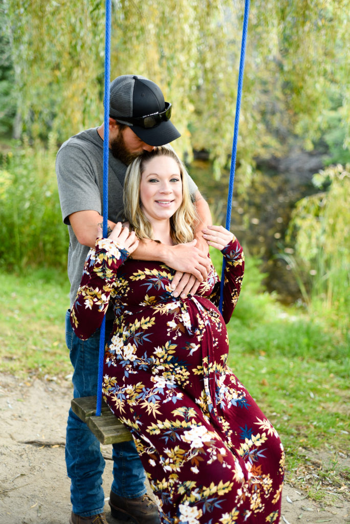 mom to be sitting on a swing. dad to be kissing her head