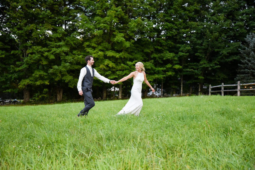 bride and groom walking in field holding hands
