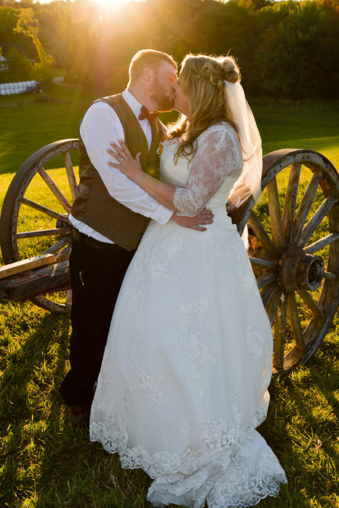 bride and groom kissing against a wagon