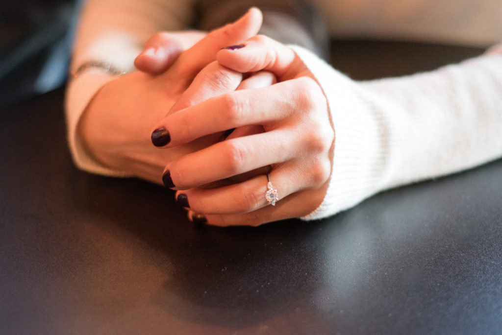 close up of engagement ring while couple holds hands