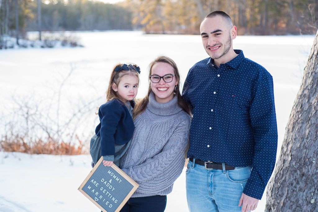family of three smiling while daughter holds sign that says mommy and daddy are getting married
