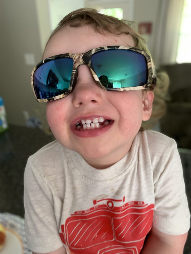 toddler wearing daddys sunglasses smiling