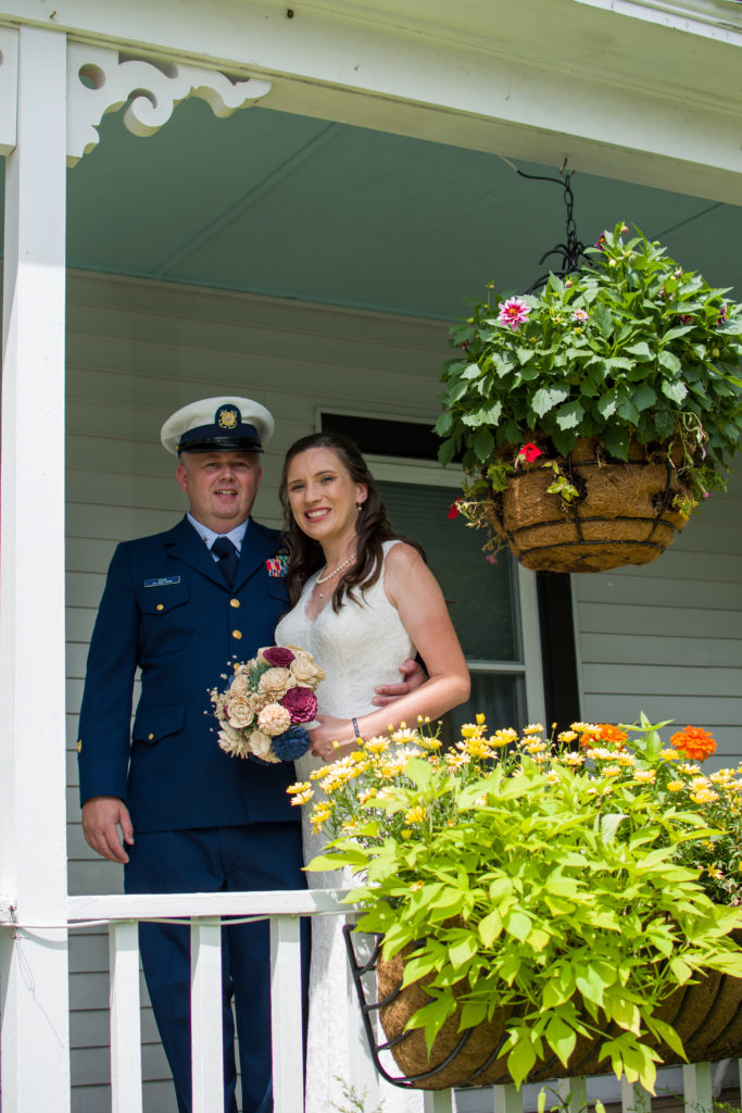 bride and groom standing on porch near flowers smiling at camera