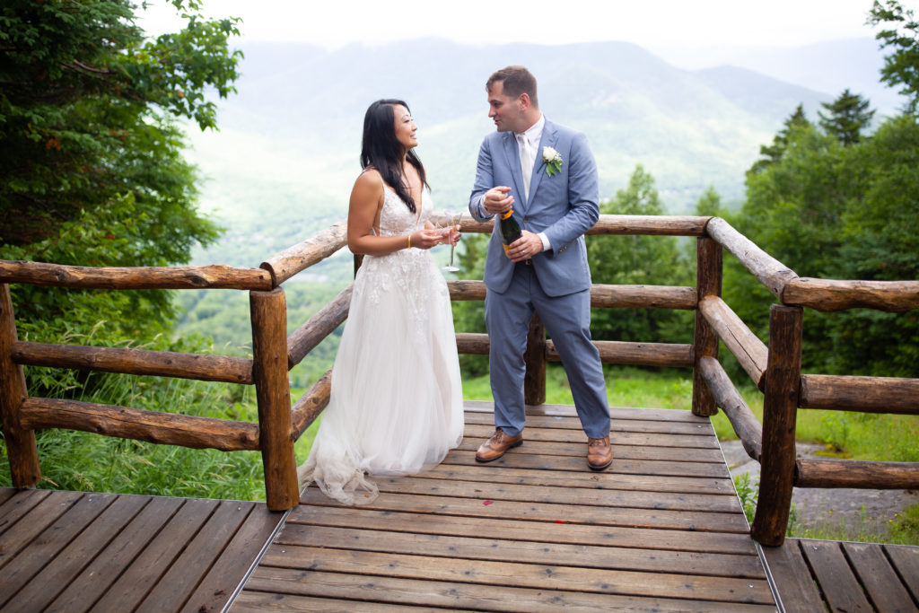groom popping champagne with bride at mountain top weddning