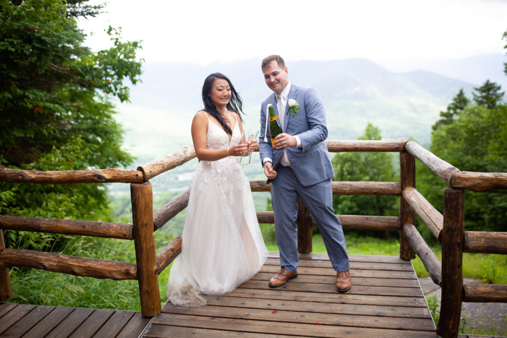 groom popping champagne with bride at mountain top wedding 