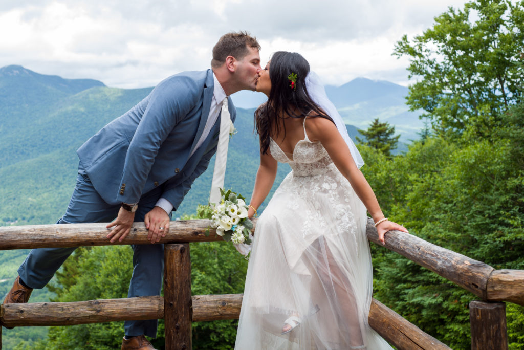 bride and groom kissing while sititng on the railing of a mountain top wedding