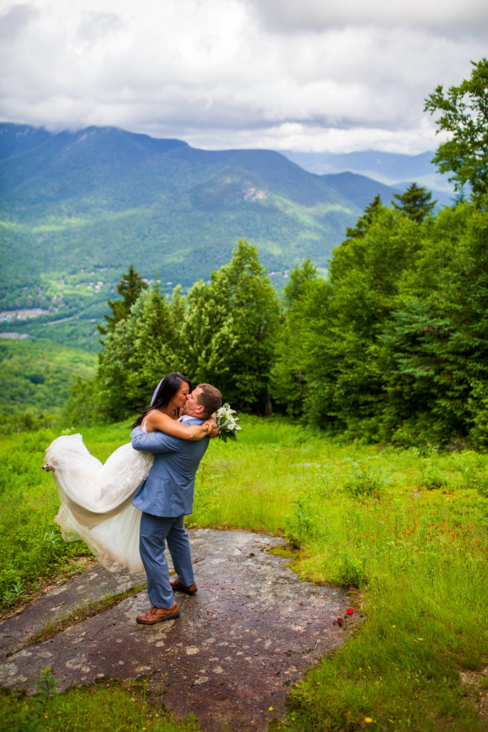 groom picking up bride and kissing with mountains in the background