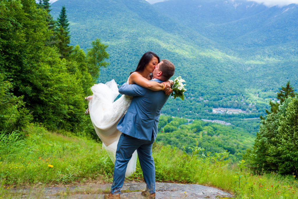 groom picking bride up and kissing at mountain top wedding