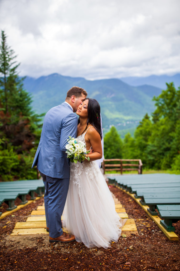groom whispering in bride's ear and bride smiling at mountain top wedding