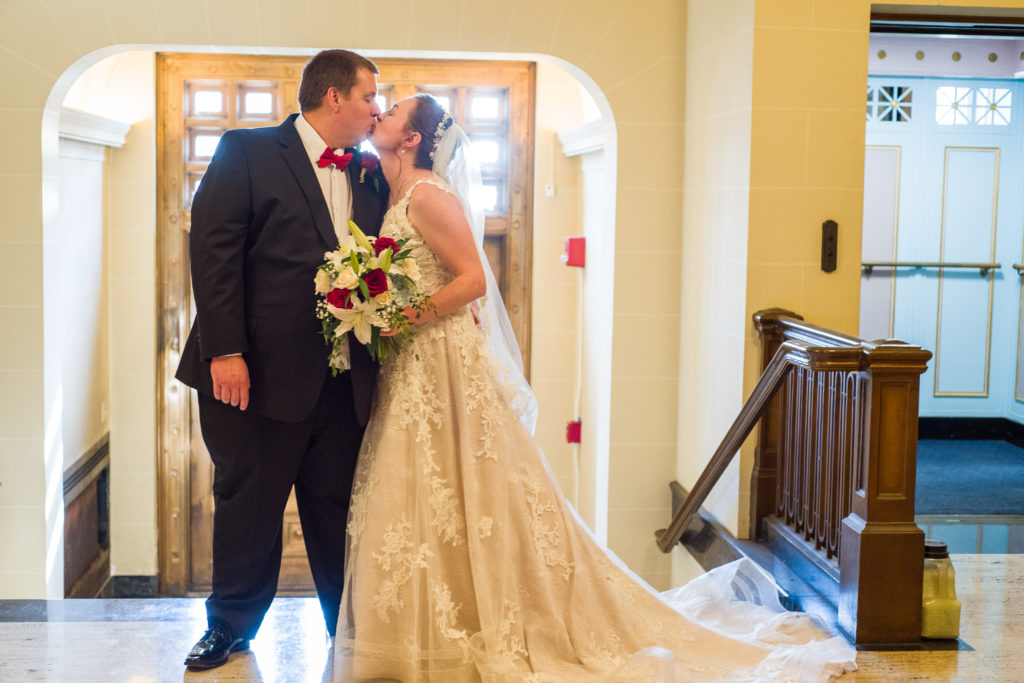 bride and groom kissing in front of stairs at masonic temple