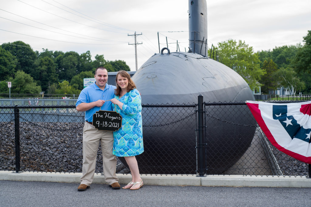 bride and groom holding save the date sign in front of the submarine