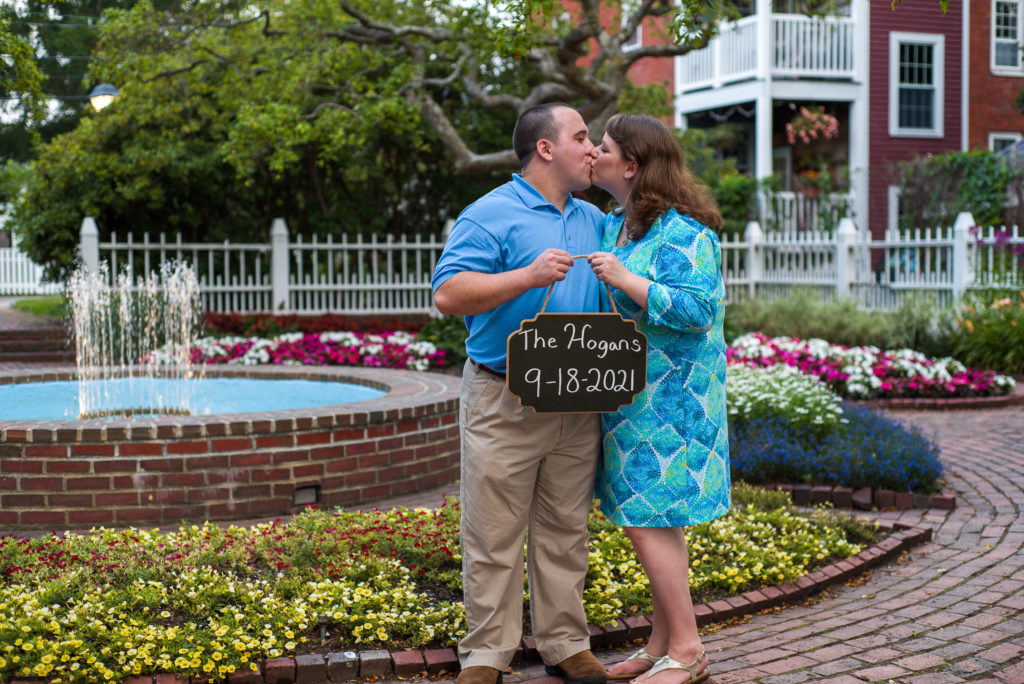 bride and groom kissing while holding save the date sign at prescott park 