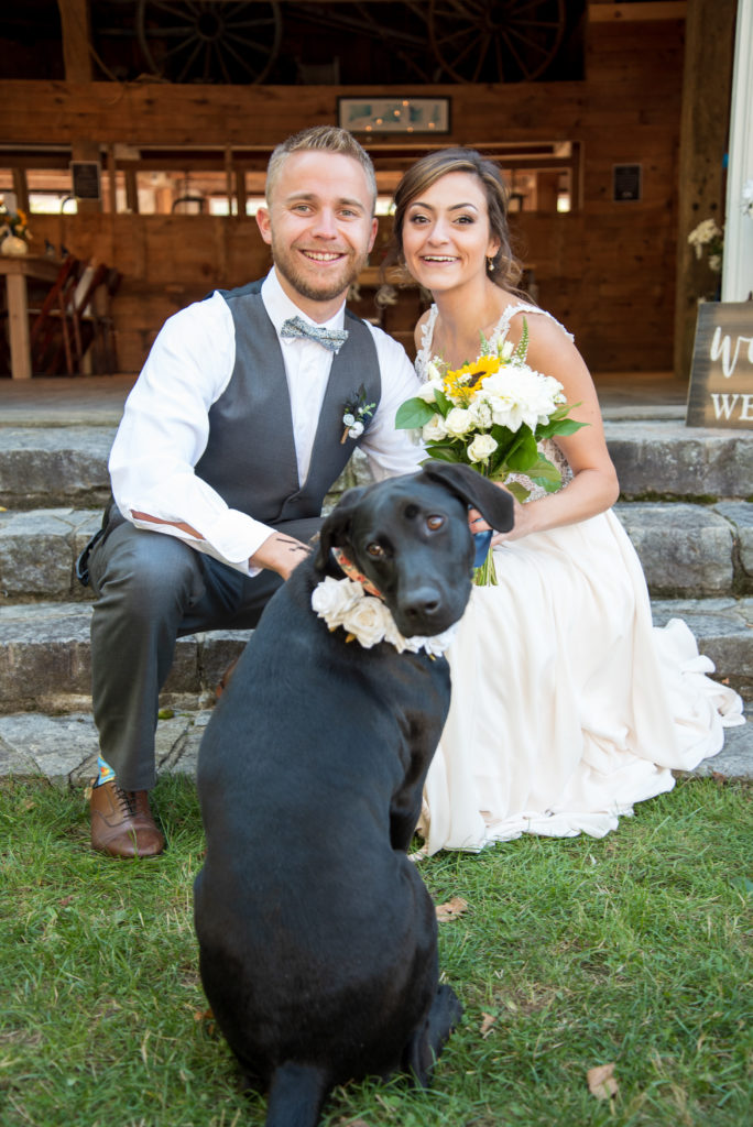 bride and groom sitting with their puppy flower girl, all smiling at the camera