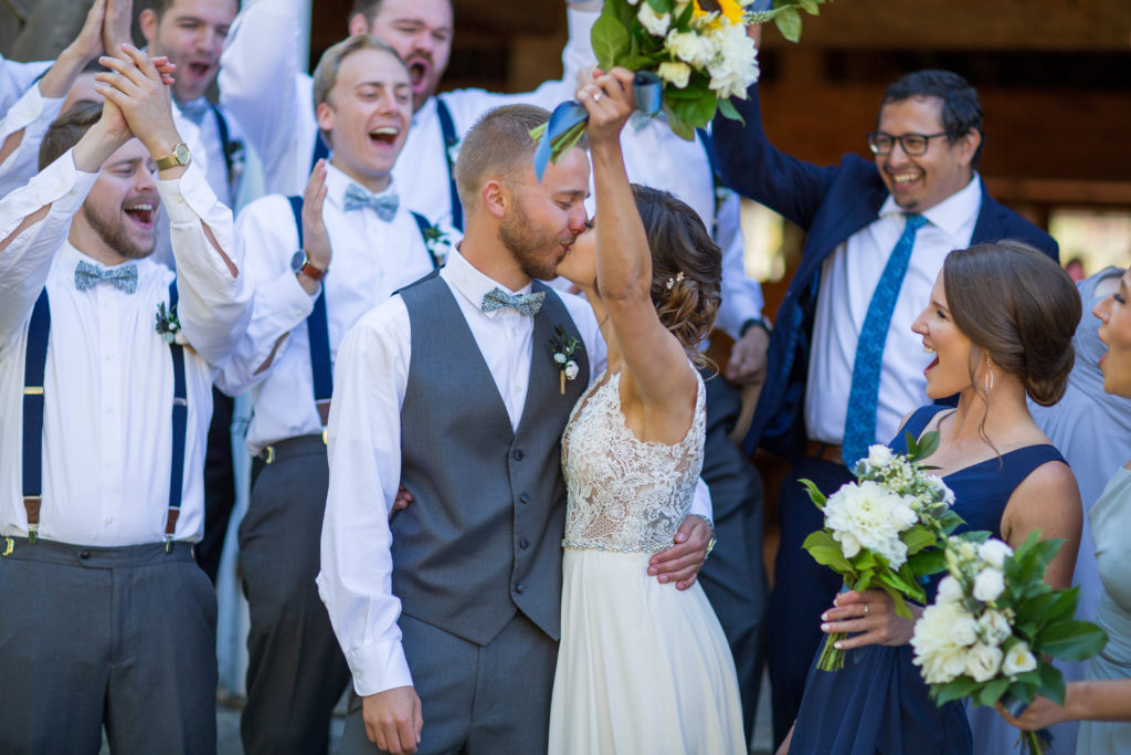 bride and groom kissing with bridal party cheering around them