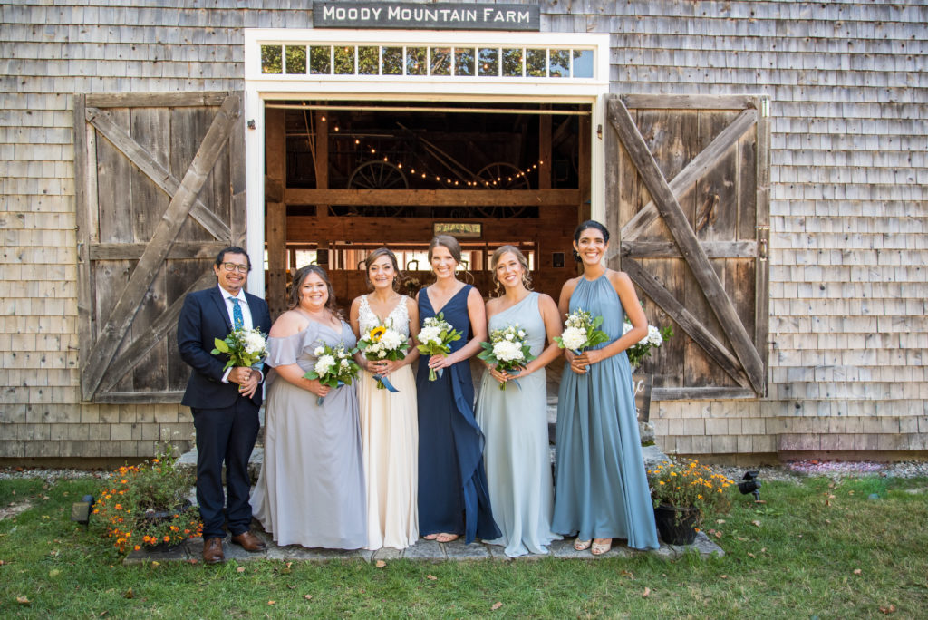 bride with her bridesmaids and bridesman in front of the barn at moody mountain farm at a fall wedding in NH