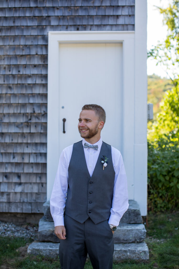 groom looking away at his bride smiling while standing in front of the barn at moody mountain farm in fall wedding NH