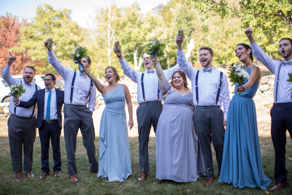 bridal party cheering their drinks as the bride and groom kiss