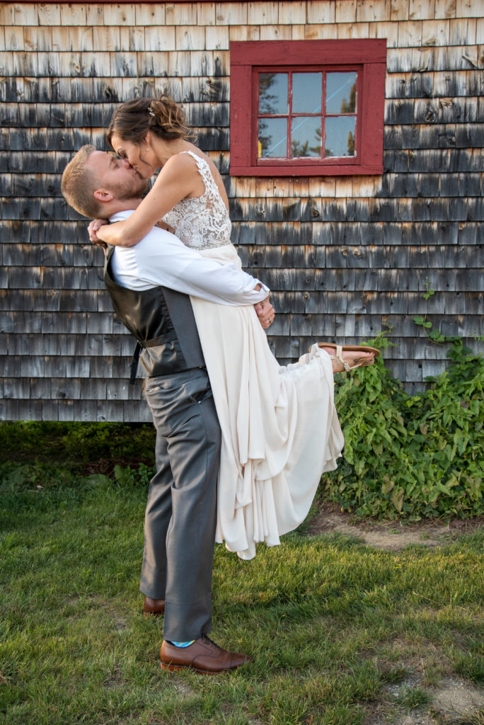 groom picking up bride and kissing in front of a Barn at Moody Mountain Farm Wedding