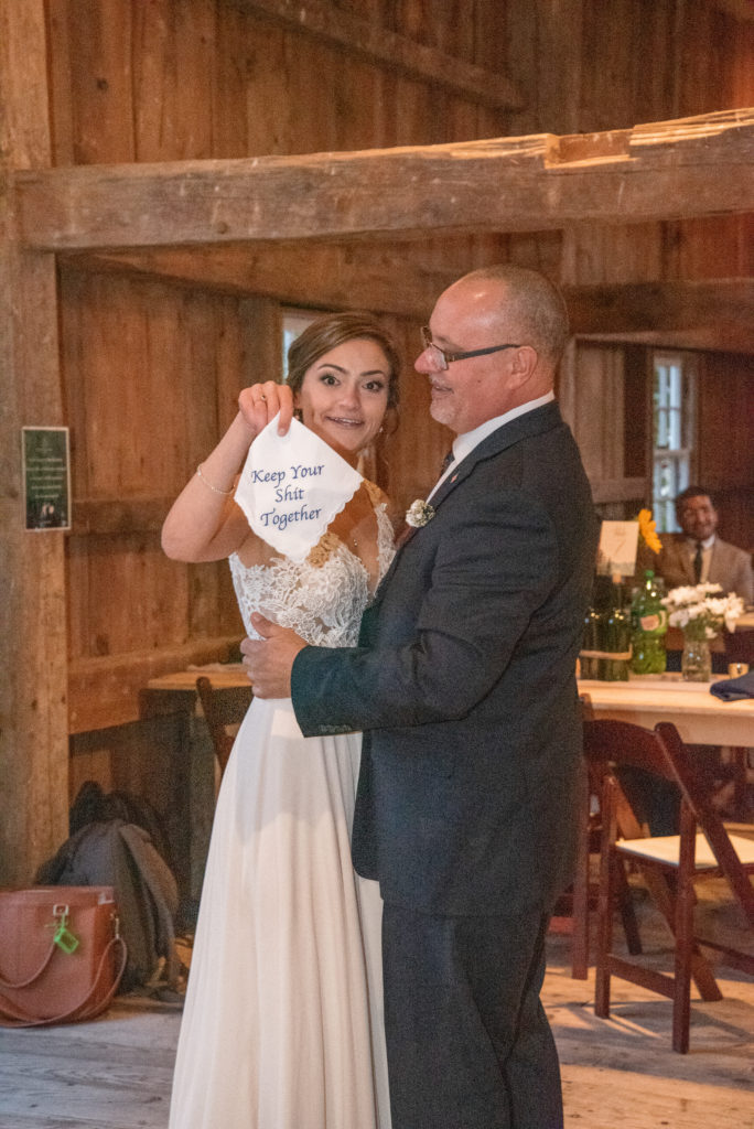 bride and her father dancing as she holds up a napkin that says "keep your shit together"