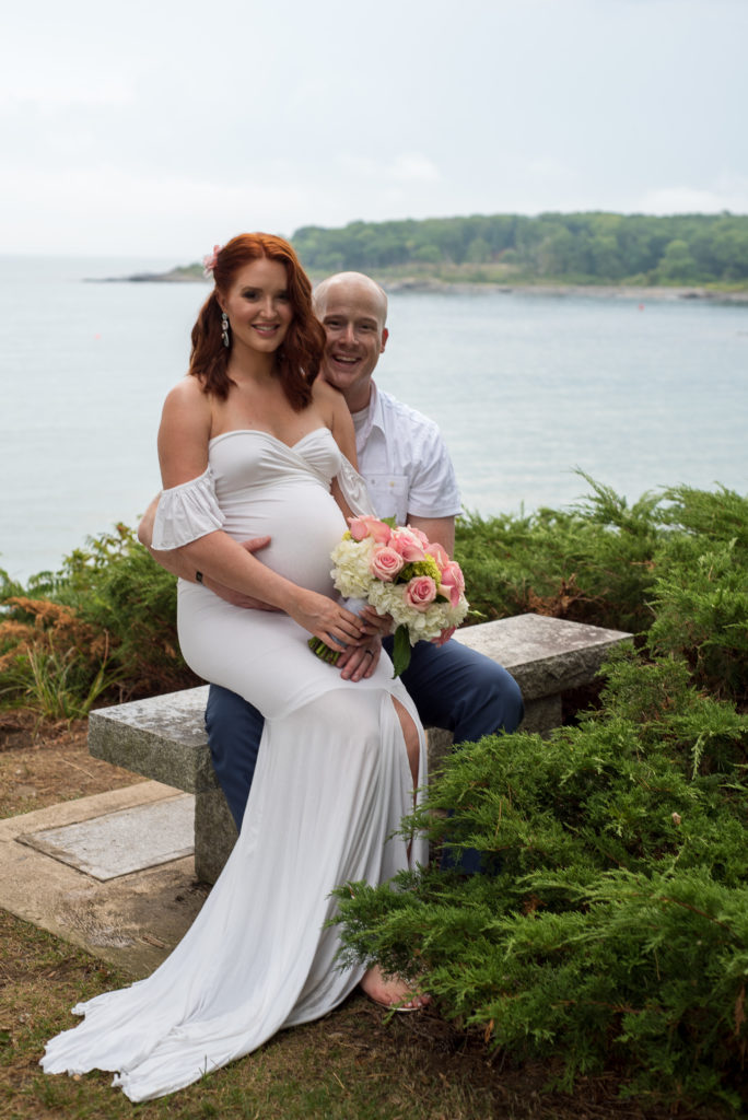 bride sitting on groom's lap on a bench in front of the ocean 