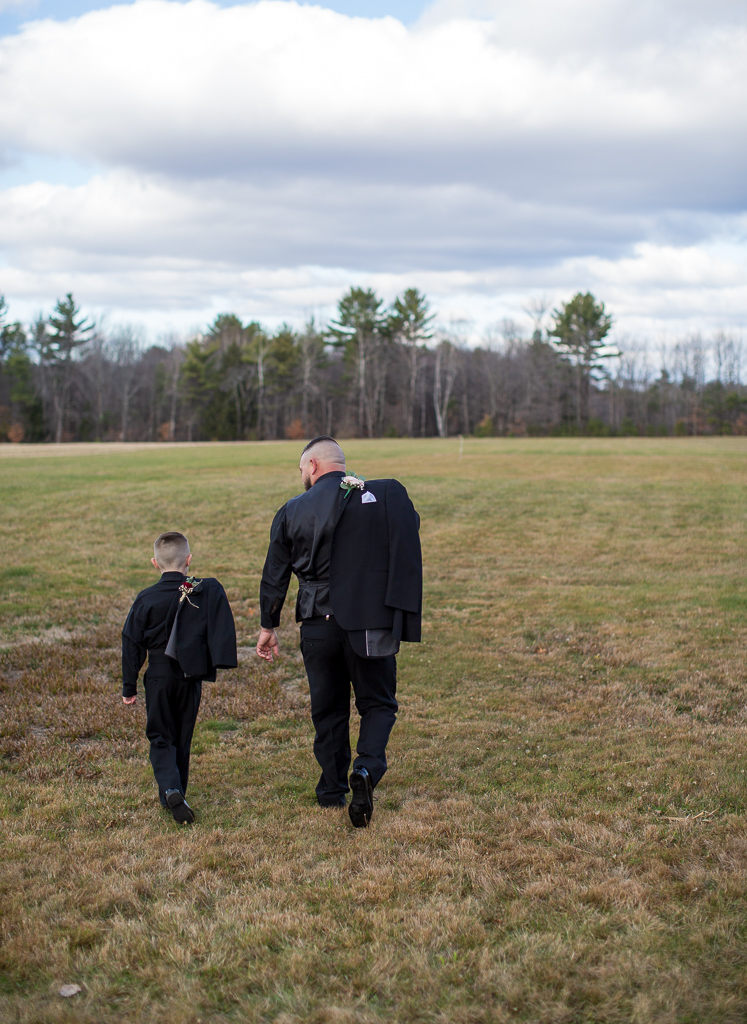 groom and his son walking away with jackets over their shoulder in a field at Whitney Farm Estate