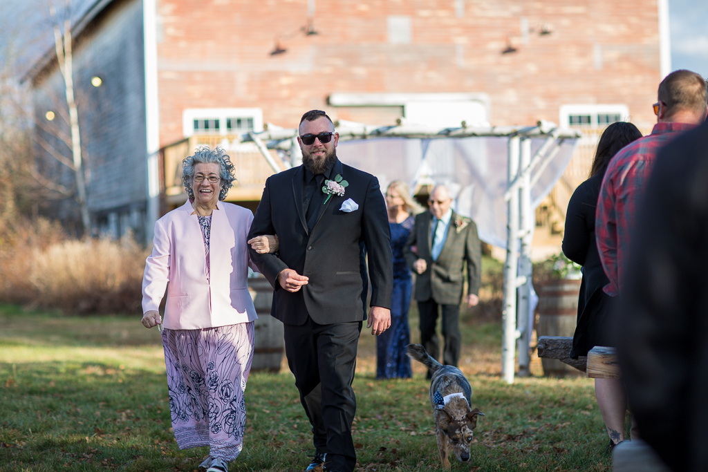 Groom walking down the aisle with his mom with the barn in the background