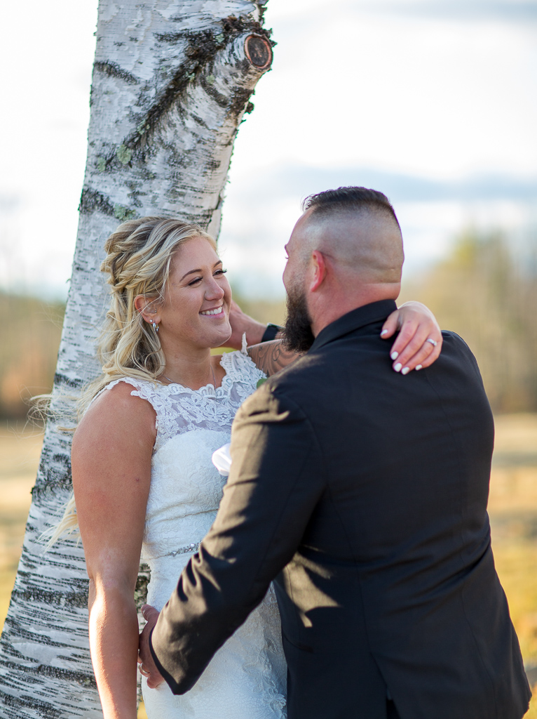 bride leaning against a white birch tree while groom looks into her eyes