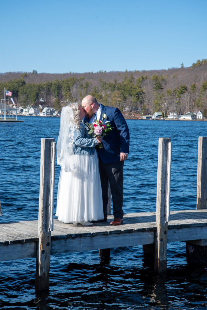 bride and groom kissing on the dock with the lake behind them
