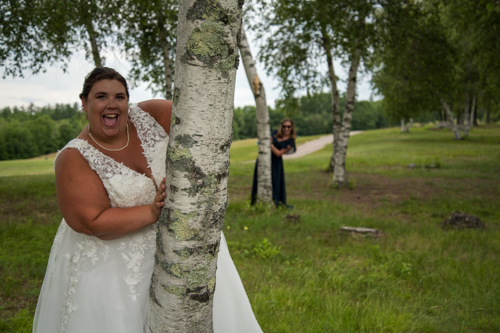 bride and maid of honor hiding behind white birch trees peaking out from behind