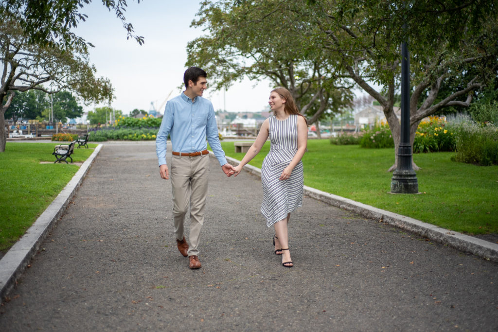 bride and groom holding hands and smiling at each other as they walk down the road at prescott park engagement session