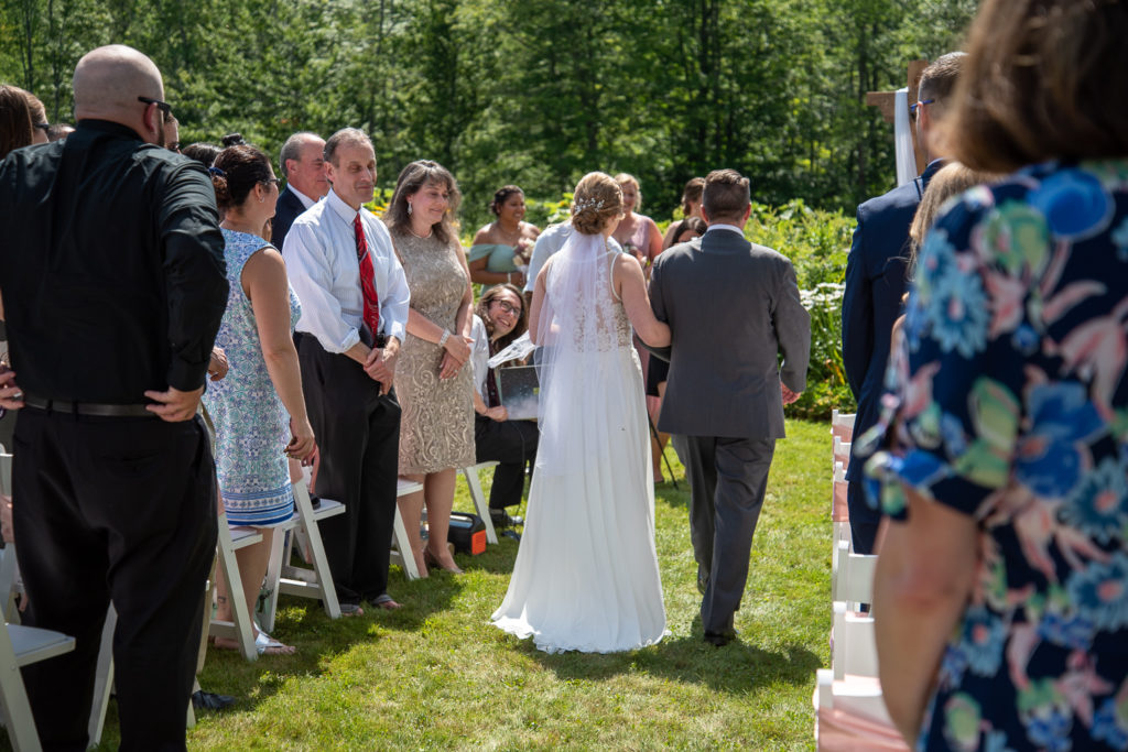 back view of bride walking with her dad down the aisle in a flower garden ceremony space 