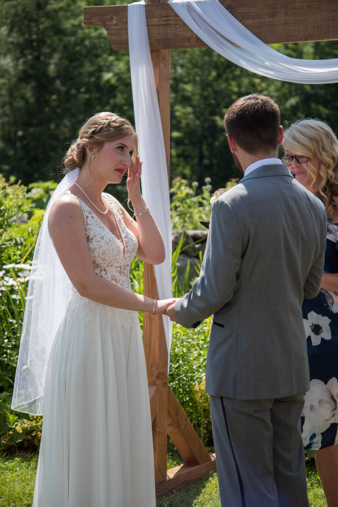 bride wiping away a tear during the ceremony at NH summer barn wedding