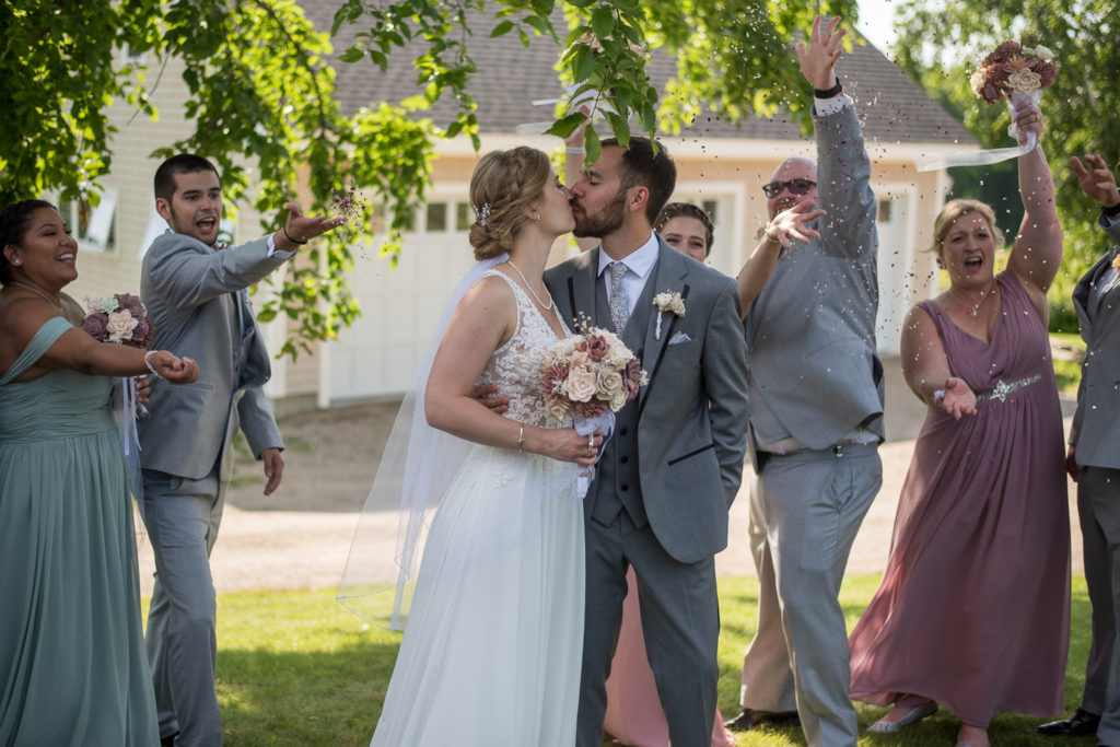 bride and groom kissing as bridal party throws confetti 