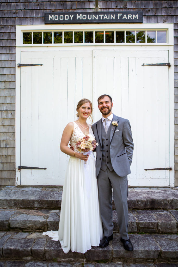 bride and groom posing in front of the barn at Barn at Moody Mountain Farm at NH summer barn wedding