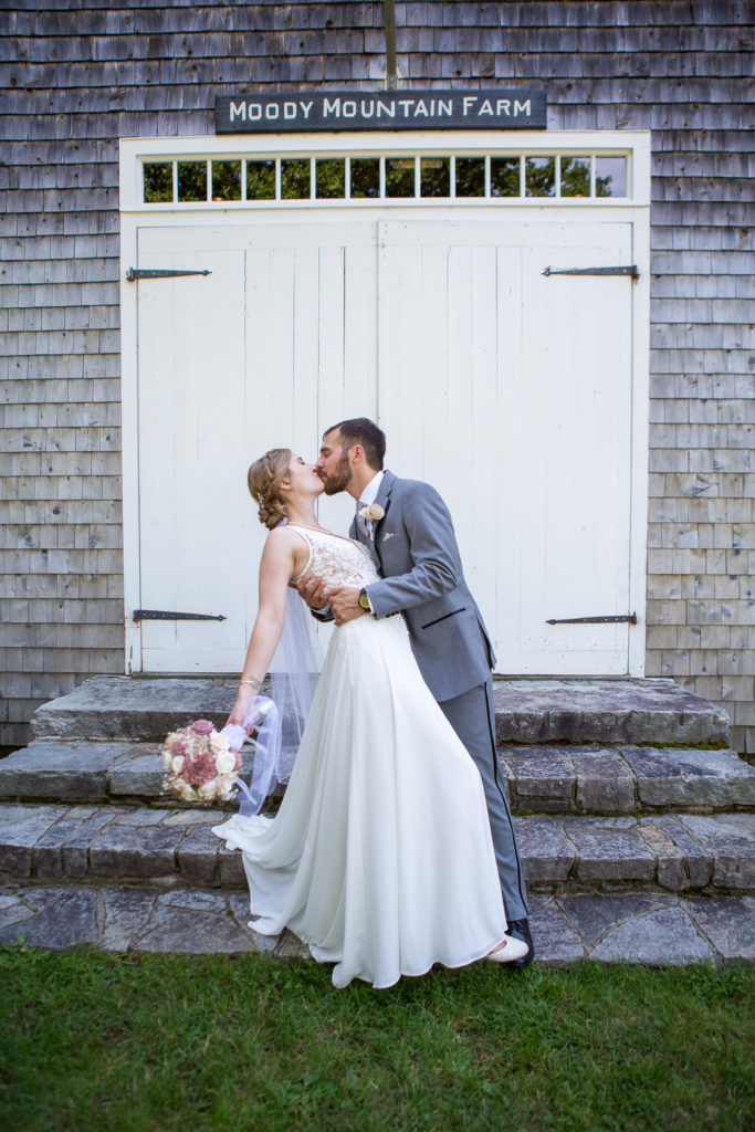 groom dipping bride to kiss her in front of the barn at NH summer barn wedding