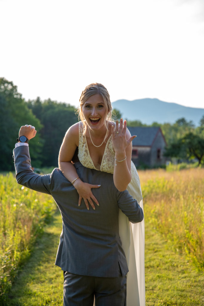 groom carrying bride over his shoulder with mountains in the background at NH summer barn wedding
