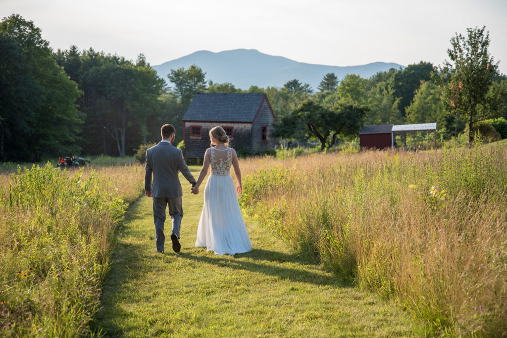 bride and groom holding hands walking towards the mountains at NH summer barn wedding
