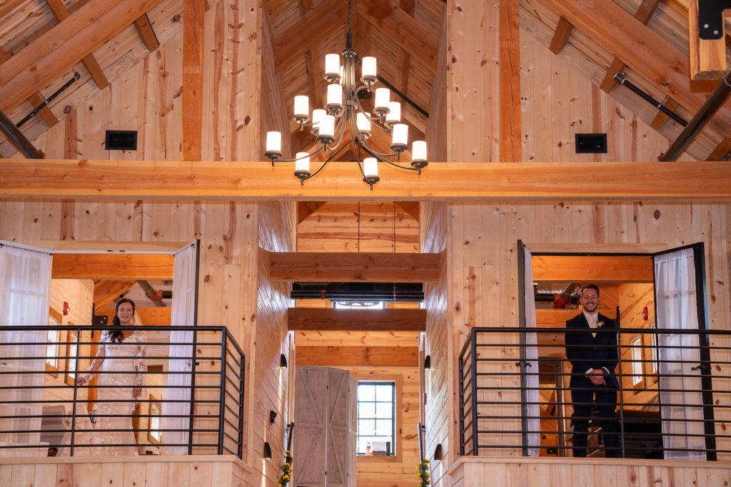 bride and groom standing in opposite balconies before first look at fall wedding at the barn